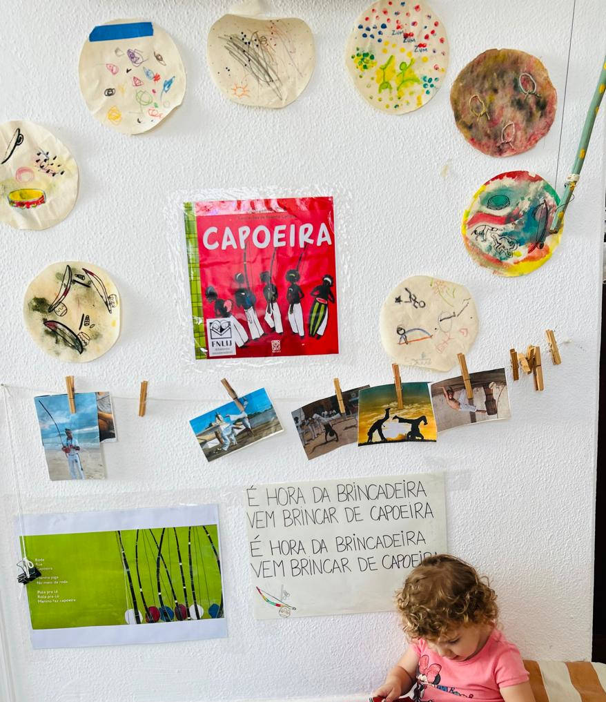 Mural com pinturas circulares feitas pelas crianças e fotos de uma atividade de capoeira